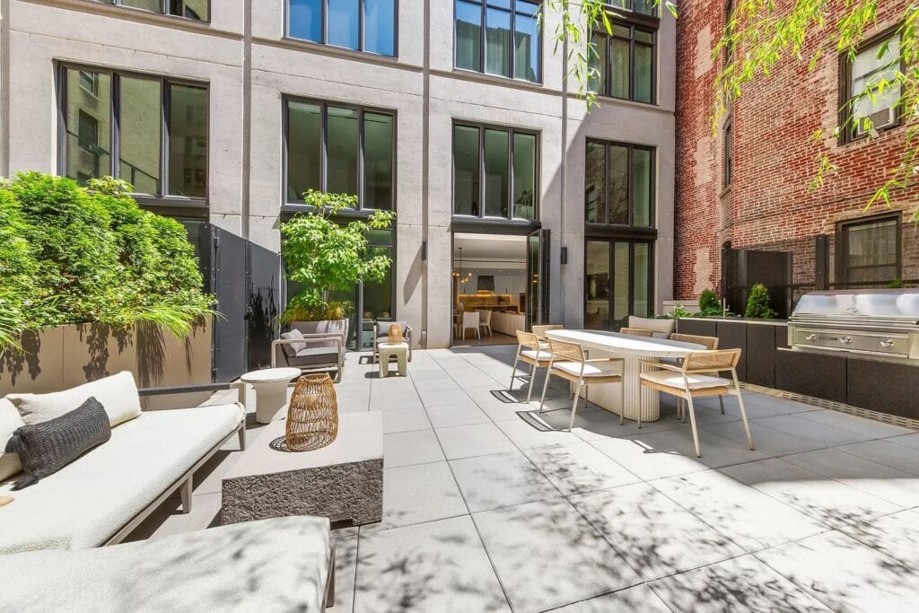 NYC rooftop outdoor kitchen with dark cabinetry, a built-in stainless steel grill, dining table, and landscaped seating area.