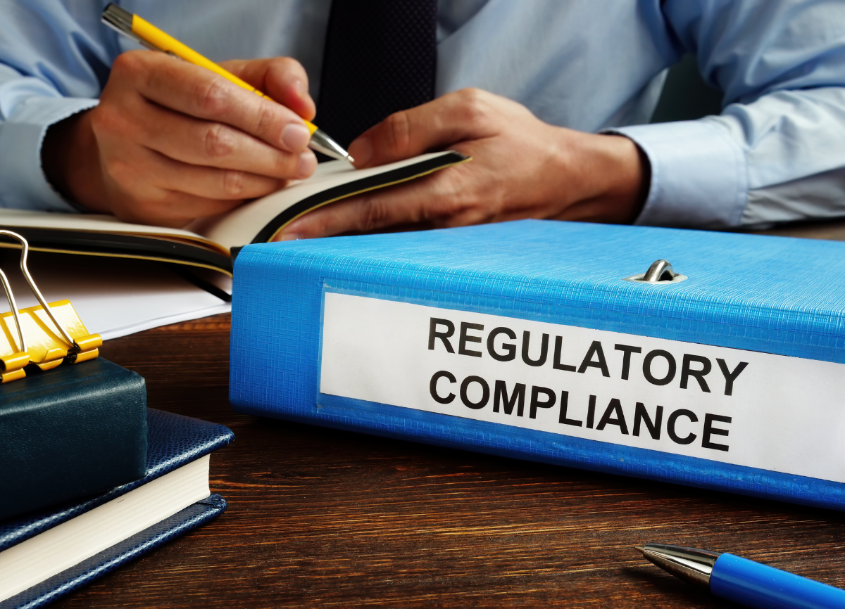 person with a notepad and binder labeled regulatory compliance