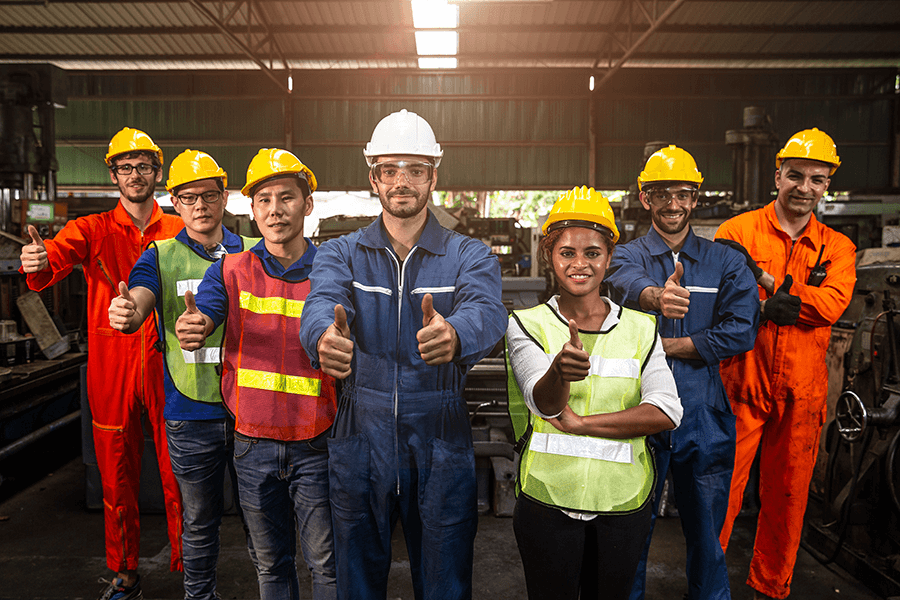 A diverse group of industrial workers wearing custom, high-visibility and durable work uniforms, giving a thumbs-up.