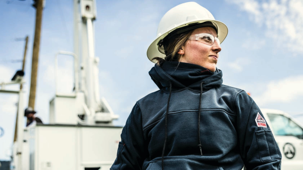Utility worker wearing a Bulwark Women’s FR Fleece Full Zip Hoodie, an NFPA 2112 compliant flame resistant jacket for cold weather