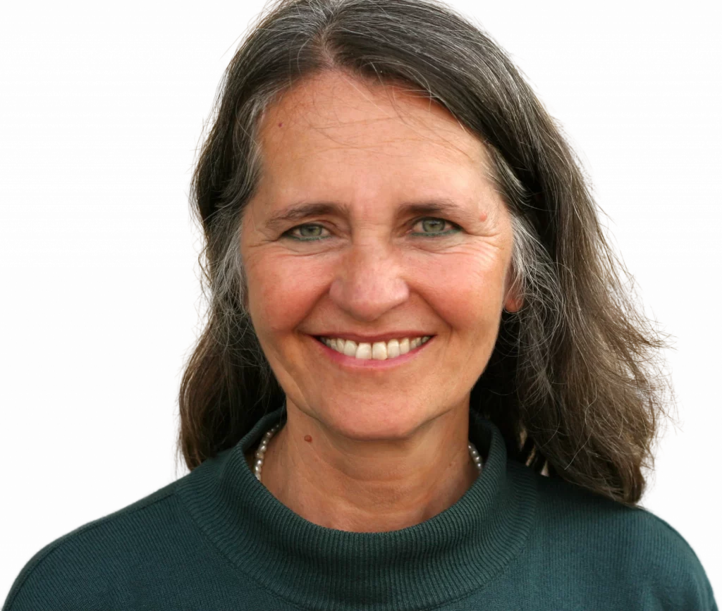 Porträt von Uschi Hedwig, Kommunikationstrainerin und Coach. Professionelle Aufnahme mit authentischem Lächeln, im grünen Rollkragenpullover mit Perlenkette. Die erfahrene Trainerin strahlt Kompetenz und Zugänglichkeit aus.