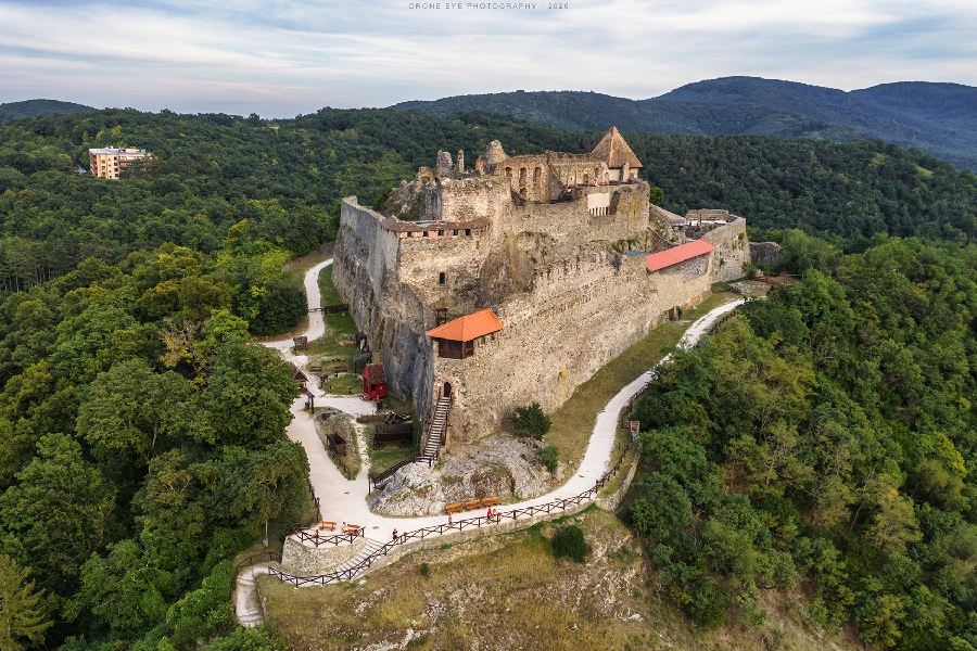 Visegrád Citadel with stone ramparts and red-roofed towers on a wooded hill.