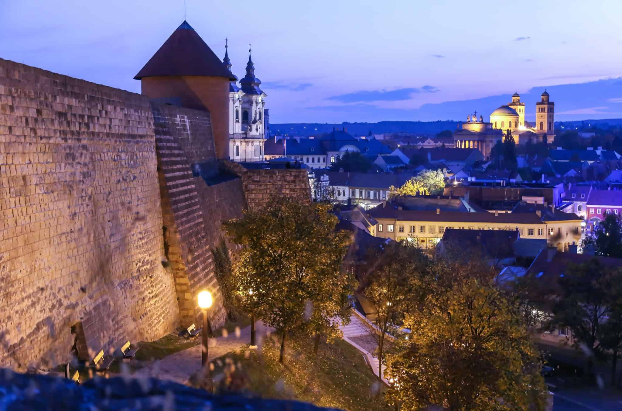Historisches Stadtbild von Budapest in der Abenddämmerung mit beleuchteten Wahrzeichen und Burgmauern.