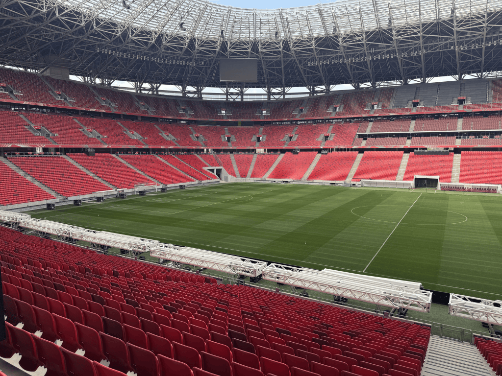 The green pitch and red stands of Puskás Aréna in daylight.