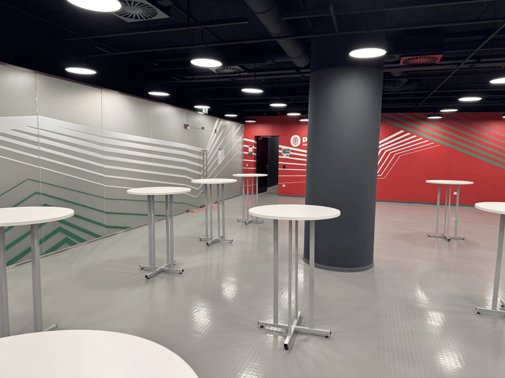 Standing tables and red and gray walls in a stadium hospitality interior.