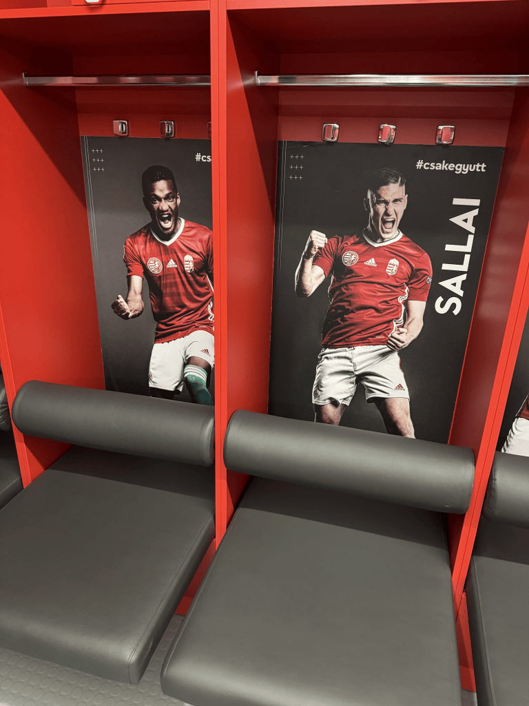 Player portraits displayed on red lockers in the Puskás Aréna dressing room.