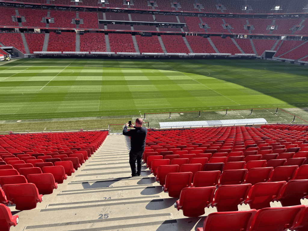 An aisle descends through red seats toward the Puskás Aréna pitch.
