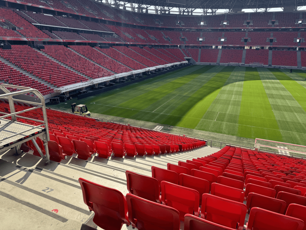 Red seating tiers and the green pitch at Puskás Aréna viewed from an aisle.