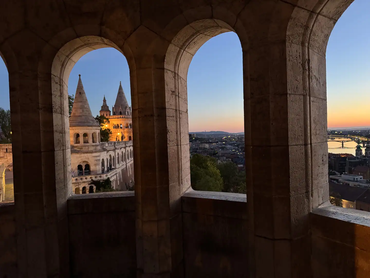 Stone arches at Fisherman’s Bastion framing a turret and the Budapest skyline at sunset.