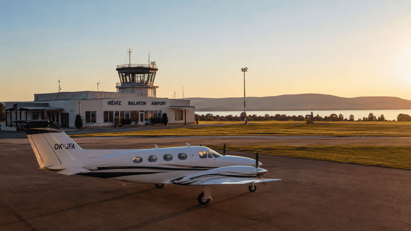 Hévíz–Balaton Airport terminal and control tower at sunset, with a small aircraft on the apron