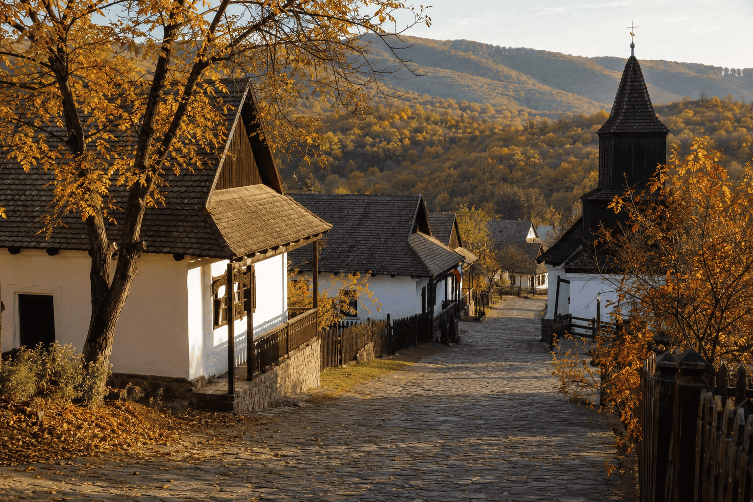 Illustration einer Dorfstraße, weiß getünchte Häuser und Bäume in Herbstfarben.
