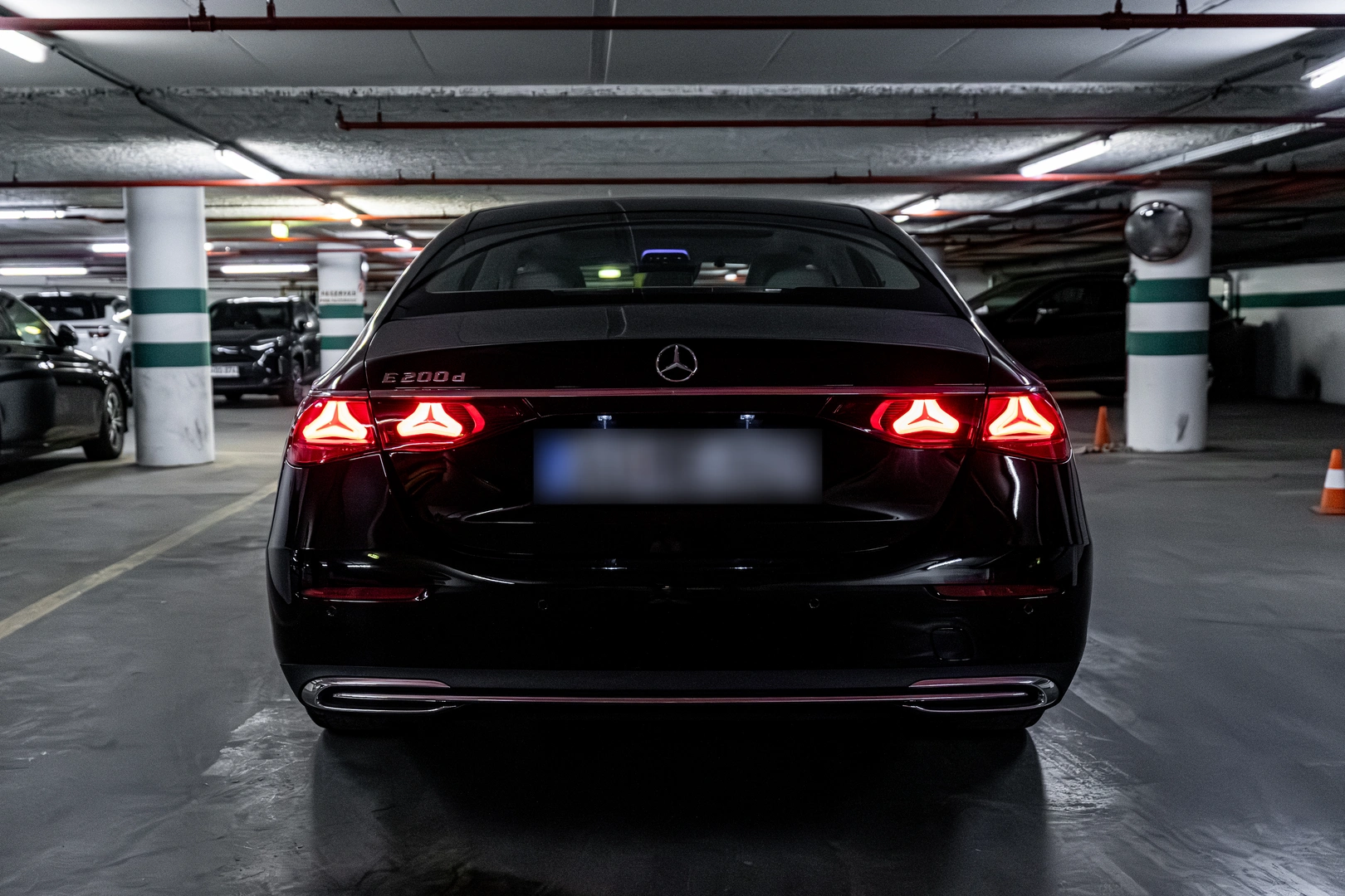 Rear view of a black Mercedes-Benz E-Class sedan with illuminated rear lamps inside a parking garage.