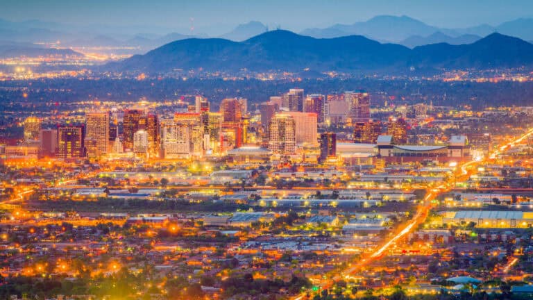 City skyline at dusk with illuminated buildings and mountain backdrop.