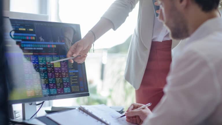 Financial professionals review stock market data on a computer screen.