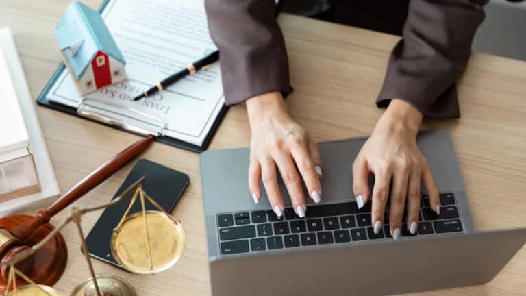 Person typing on a laptop with legal documents and a small house model nearby.