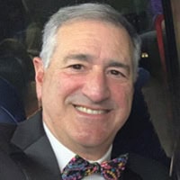 A man with gray hair smiles at the camera while wearing a suit and a colorful bow tie.