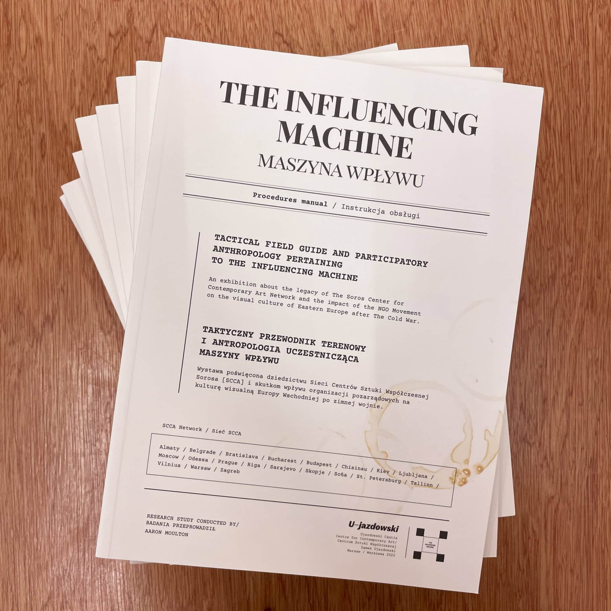 Close-up of a manual titled 'The Influencing Machine' by Maszyna Wplywu, on a wooden surface.