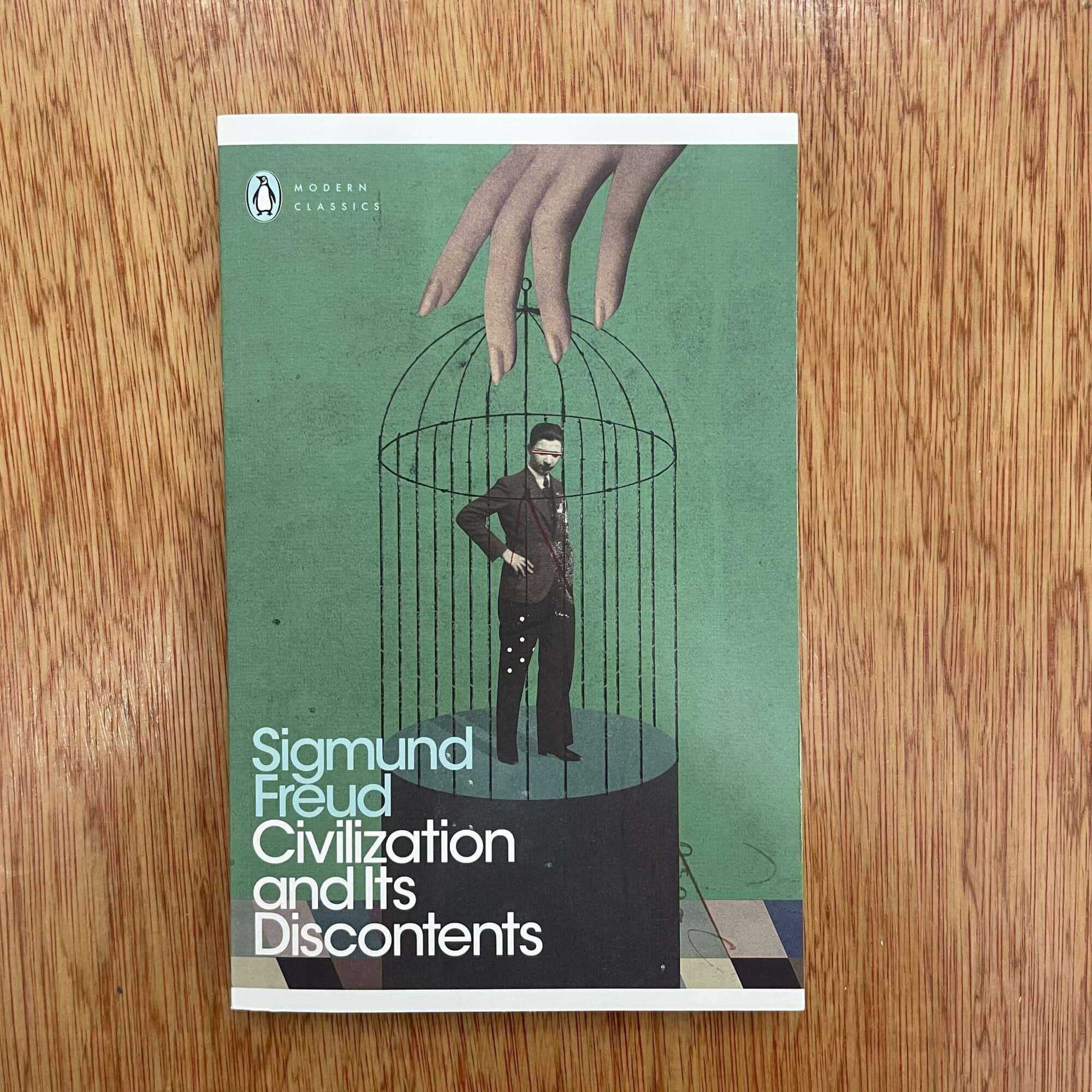 Book cover of 'Civilization and Its Discontents' by Sigmund Freud, featuring a man in a cage with a green background.