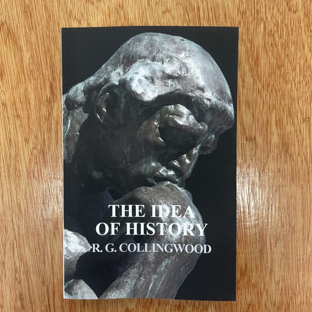 Close-up of 'The Idea of History' book by R.G. Collingwood on a wooden surface.