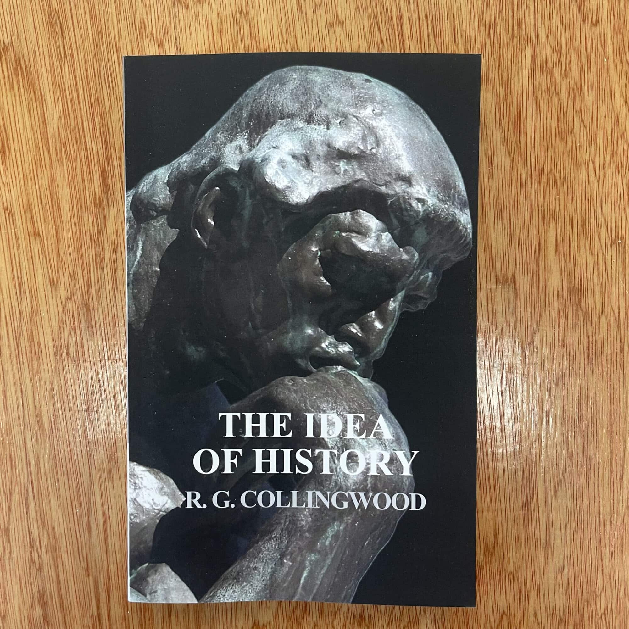 Close-up of 'The Idea of History' book by R.G. Collingwood on a wooden surface.