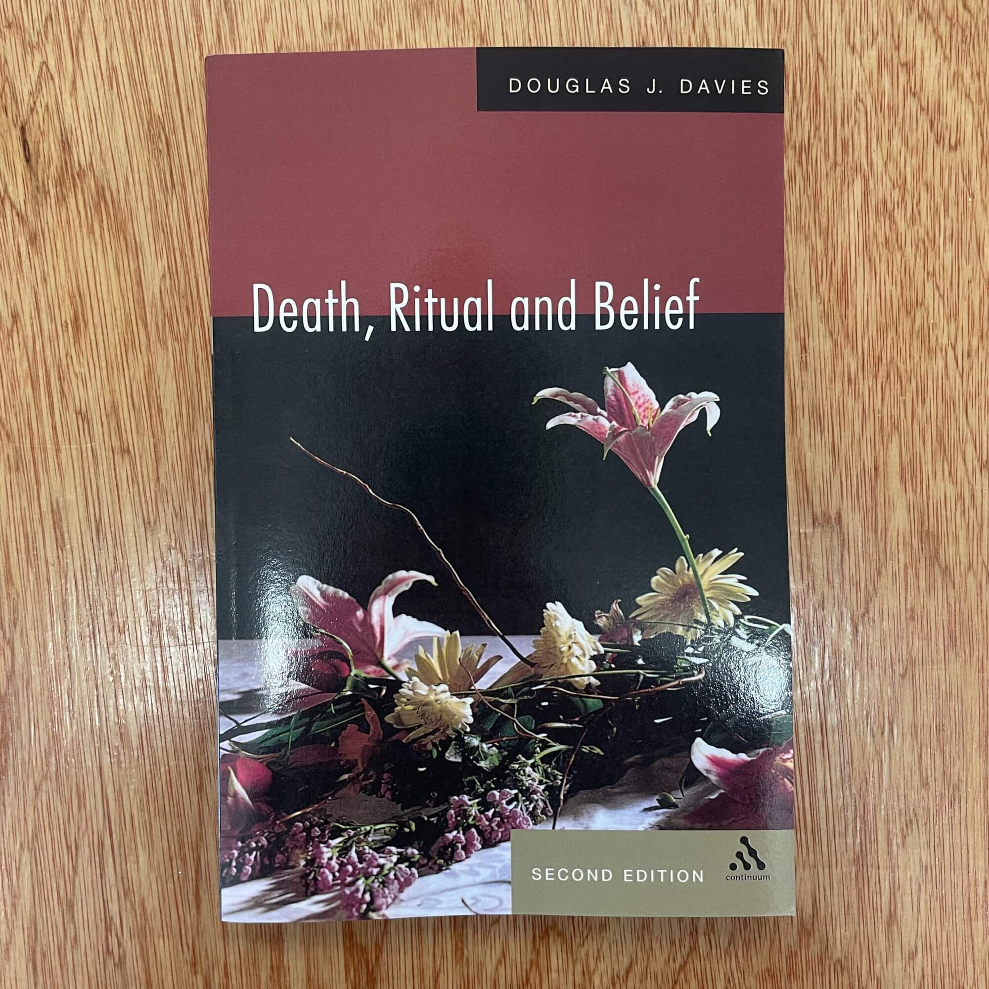 Book titled 'Death, Ritual and Belief' by Douglas J. Davies, second edition, with floral cover design, on a wooden surface.