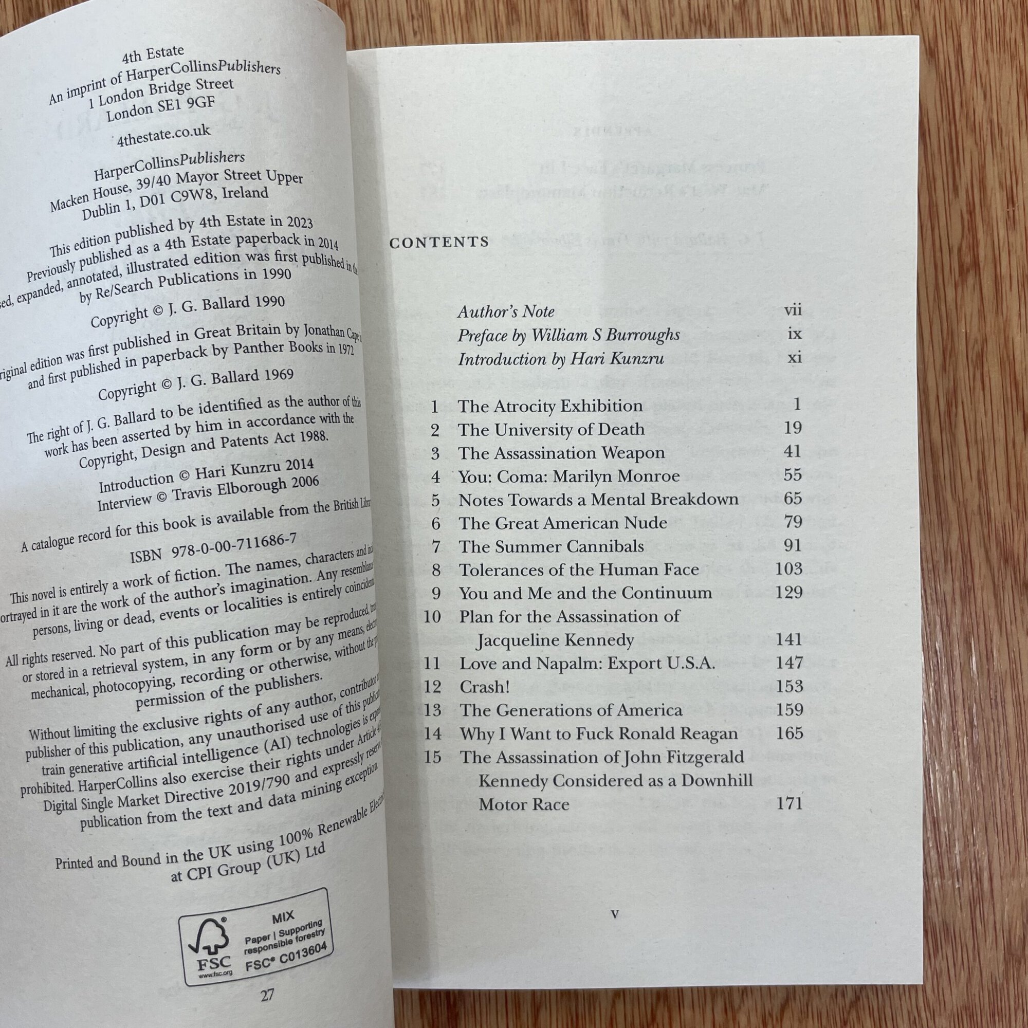 Open book with contents page, featuring titles of essays and authors, on a wooden surface.