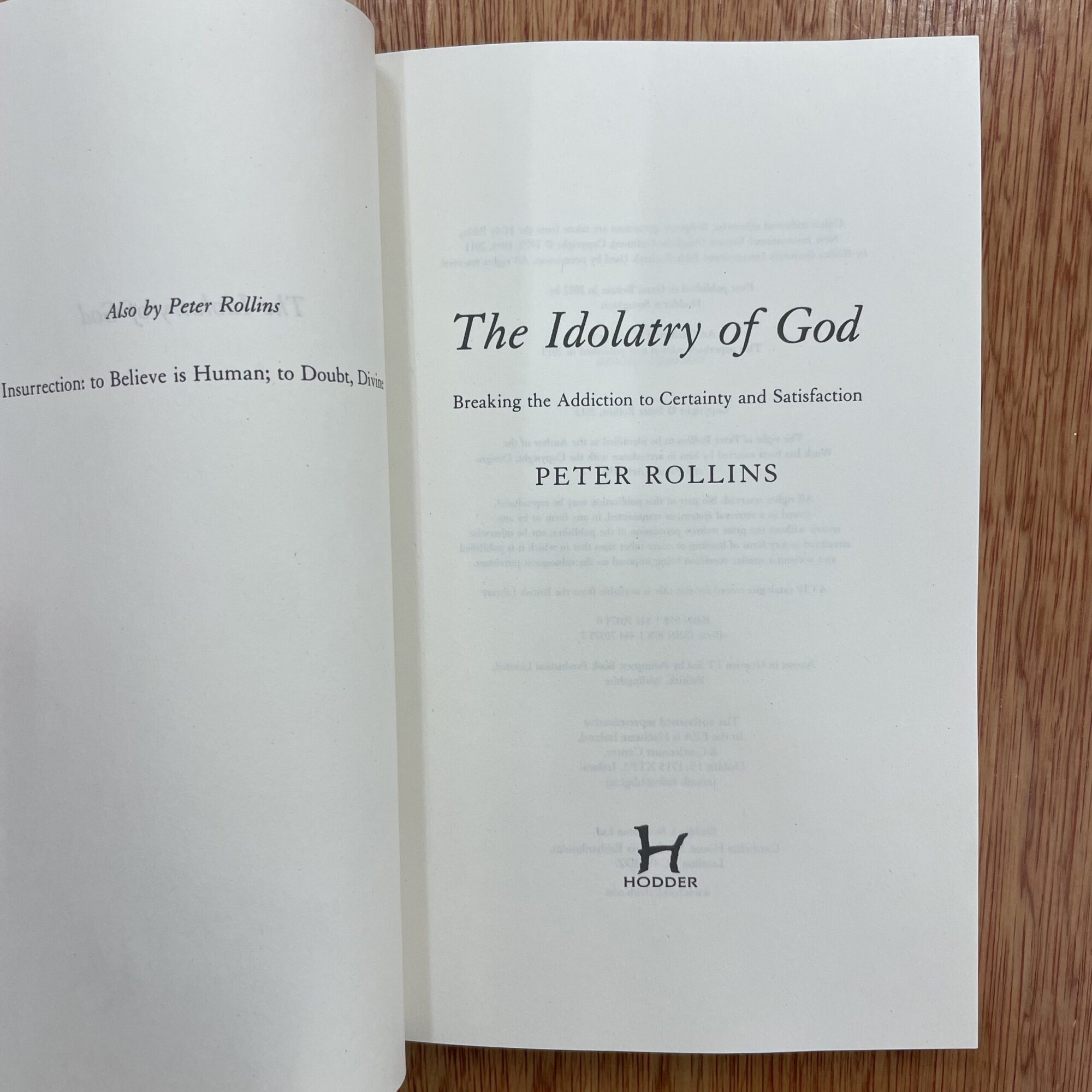 Open book titled 'The Idolatry of God' by Peter Rollins, with a wooden surface background.