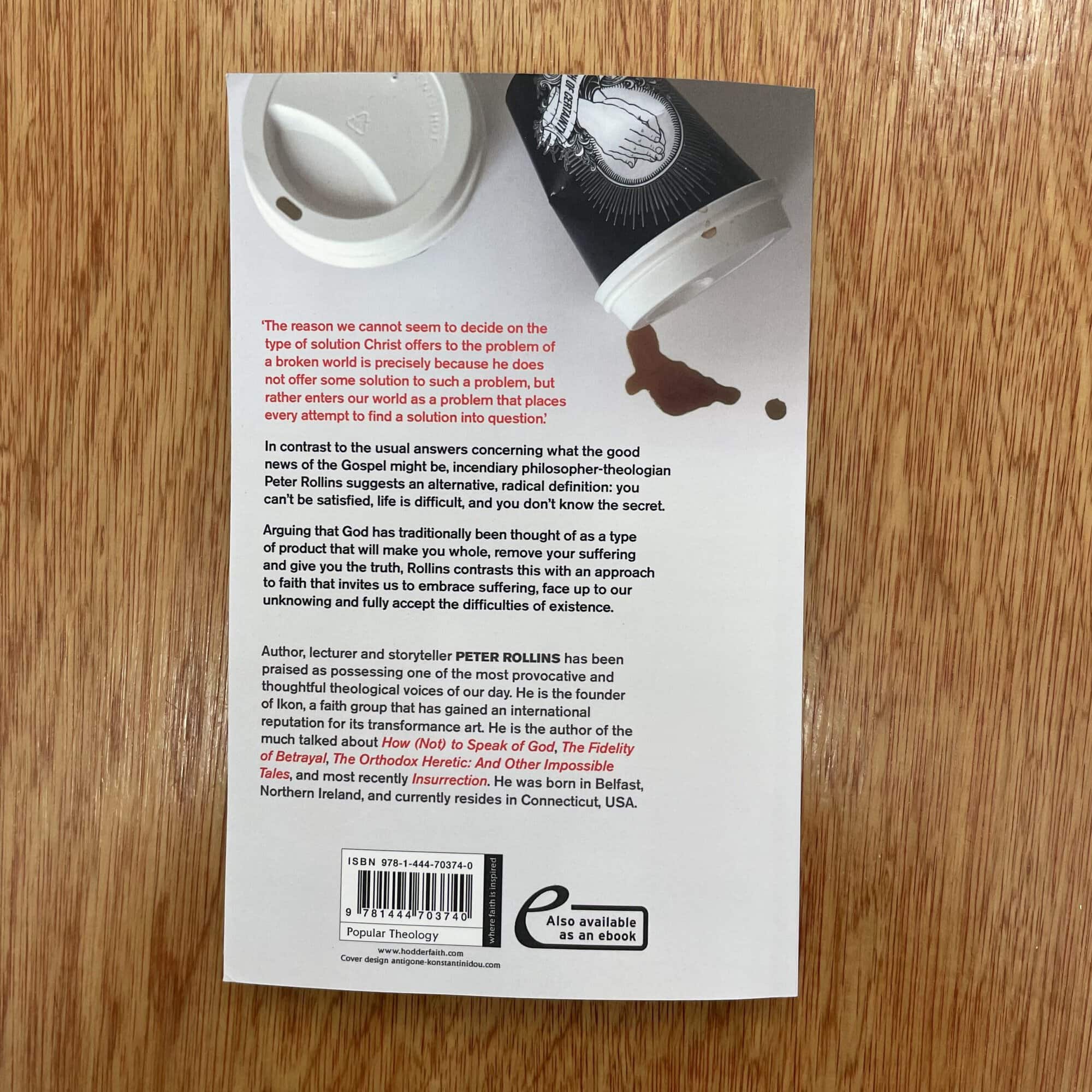 Back cover of 'The Idolatry of God' by Peter Rollins with a coffee cup and a spilled drink on a wooden surface.