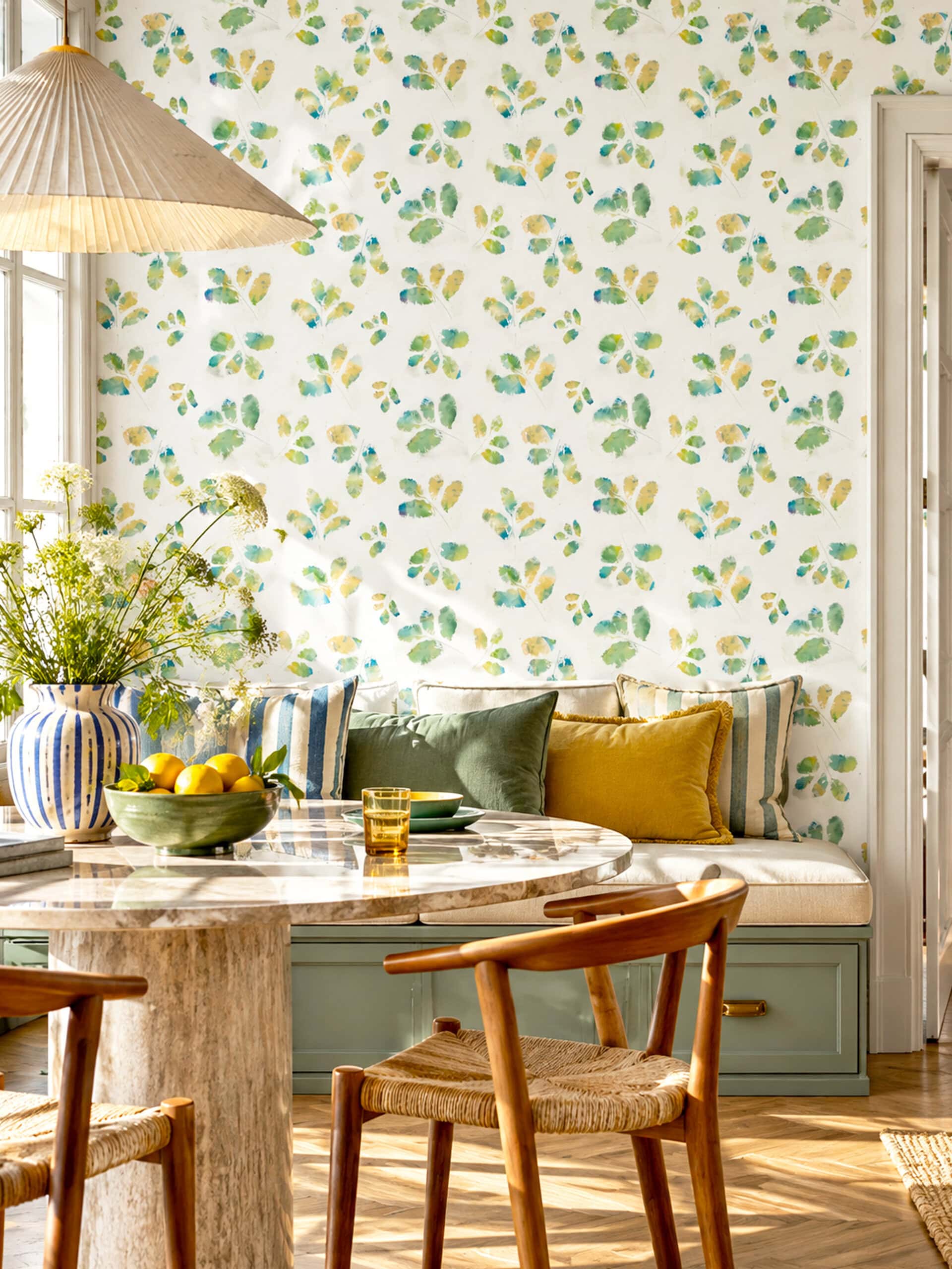 Large-scale watercolour leaf wallpaper behind a built-in banquette in a sunny breakfast nook
