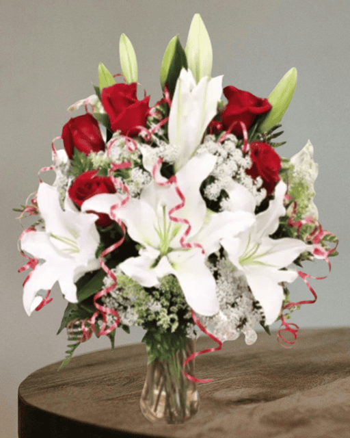 Elegant bouquet of white lilies and vibrant red roses with delicate greenery and decorative accents. Perfect for special occasions or expressing love and admiration.