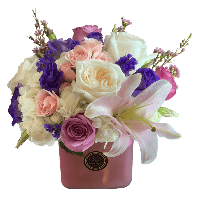 Elegant floral arrangement featuring white roses, pink roses, purple lisianthus, and white lilies in a pink cube vase. Perfect for sophisticated celebrations and heartfelt gifts.
