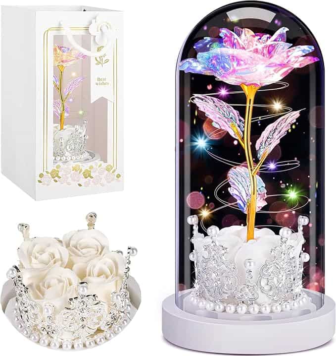 Illuminated artificial flower in glass dome with pink and purple petals, surrounded by sparkling lights and decorative silver crown base.