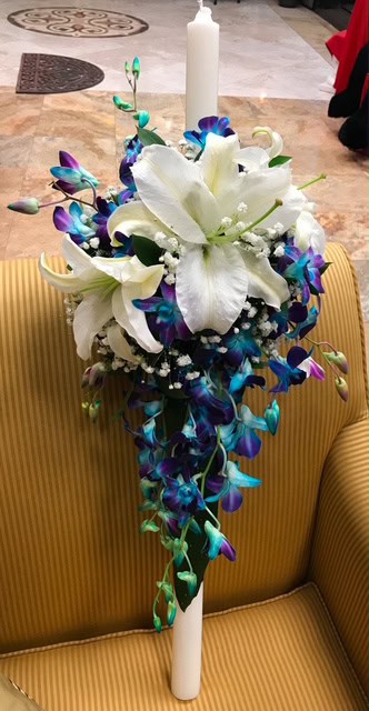 A stunning floral arrangement featuring white lilies and vibrant purple and blue orchids with a white candle, perfect for elegant events and special occasions in Las Vegas.