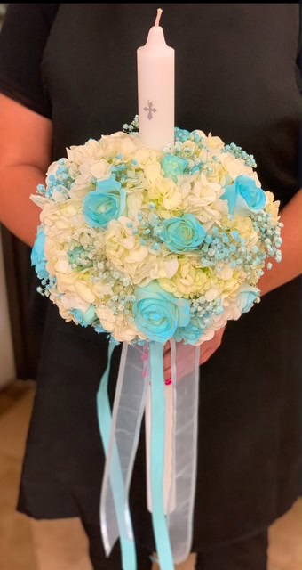 Vibrant candle centerpiece with pastel blue and white roses, hydrangeas, and ribbons, perfect for celebrations or memorials.