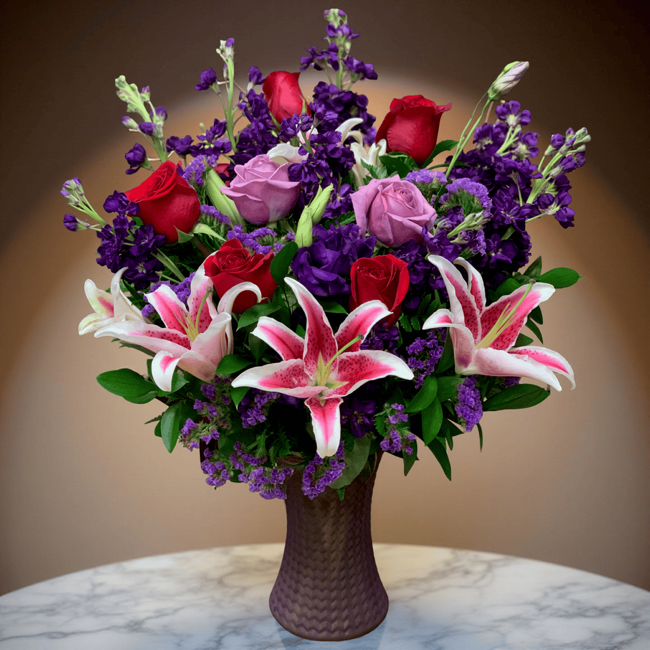Breathtaking Elegance luxury bouquet with red roses, lavender roses, pink stargazer lilies and purple stock in textured bronze vase Las Vegas florist