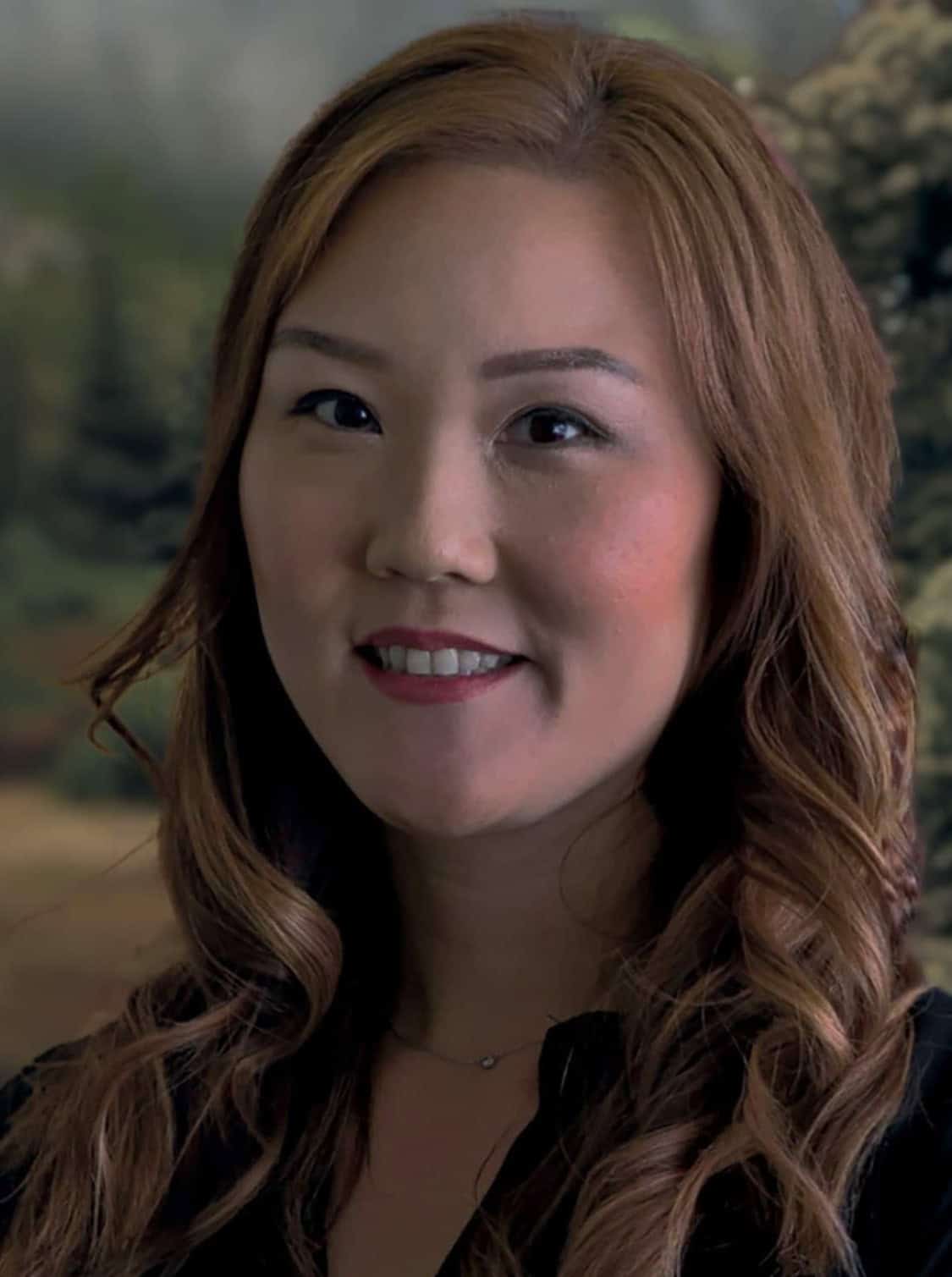 Portrait of a smiling woman with wavy hair in a natural outdoor setting.