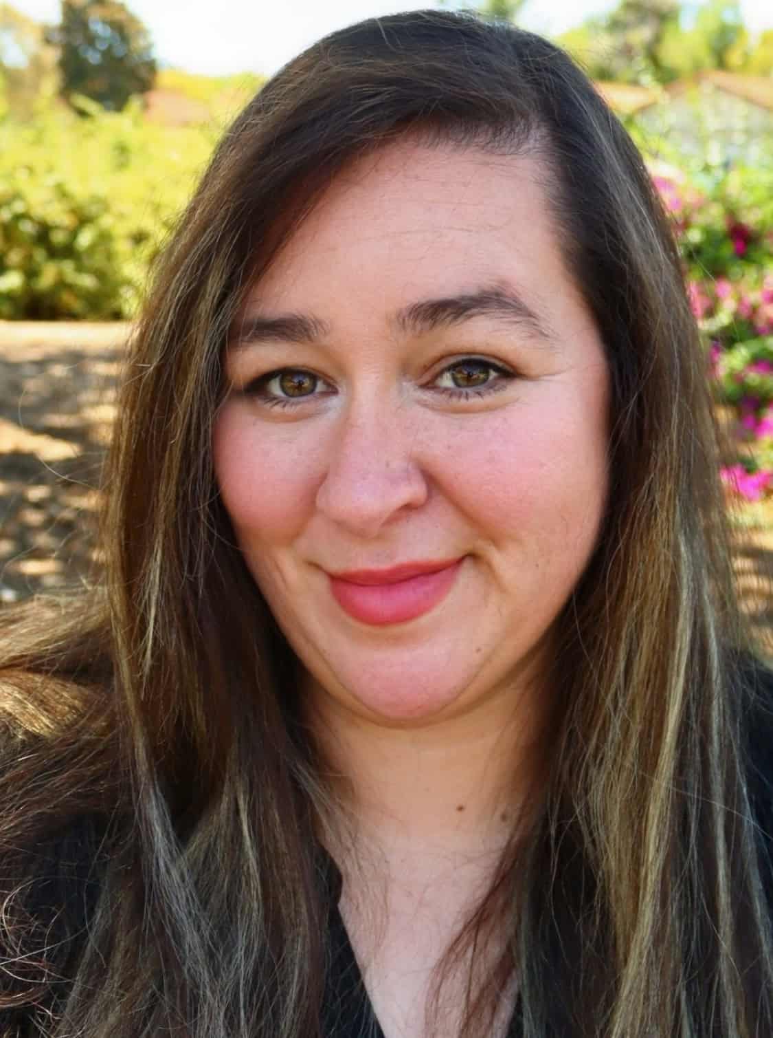 Portrait of a woman outdoors with colorful flowers in the background.