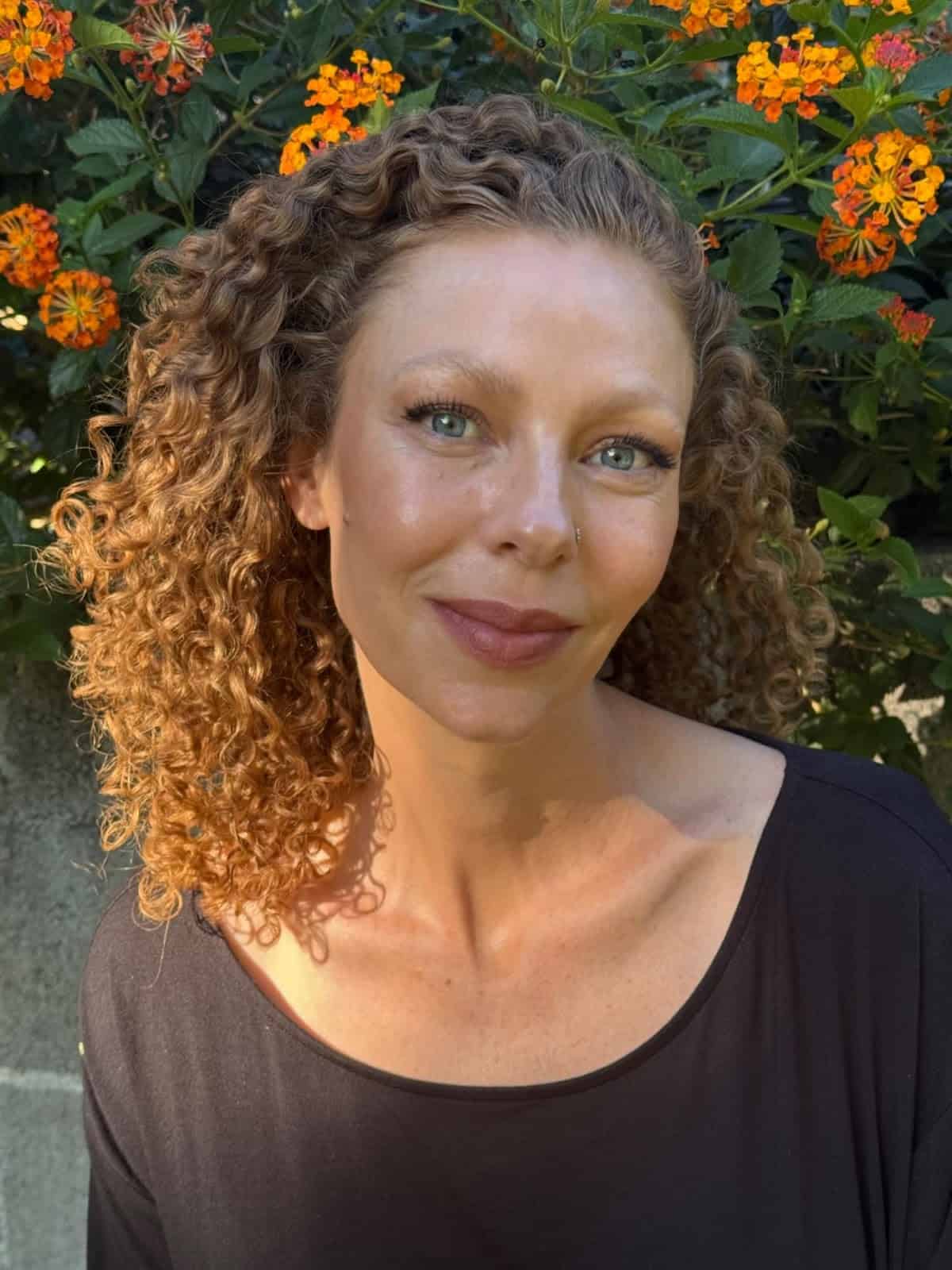 Portrait of a woman with curly hair in front of orange flowers.