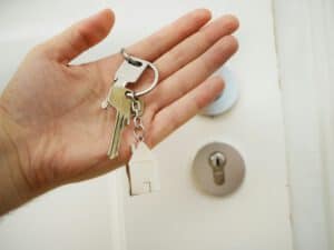 An image of an open hand holding a bunch of keys against a backdrop of a front door and door lock