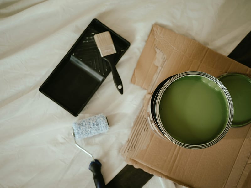 A close up of painter and decorators work bench cover with a dust sheet and showing a paint roller, tray and a can of green paint