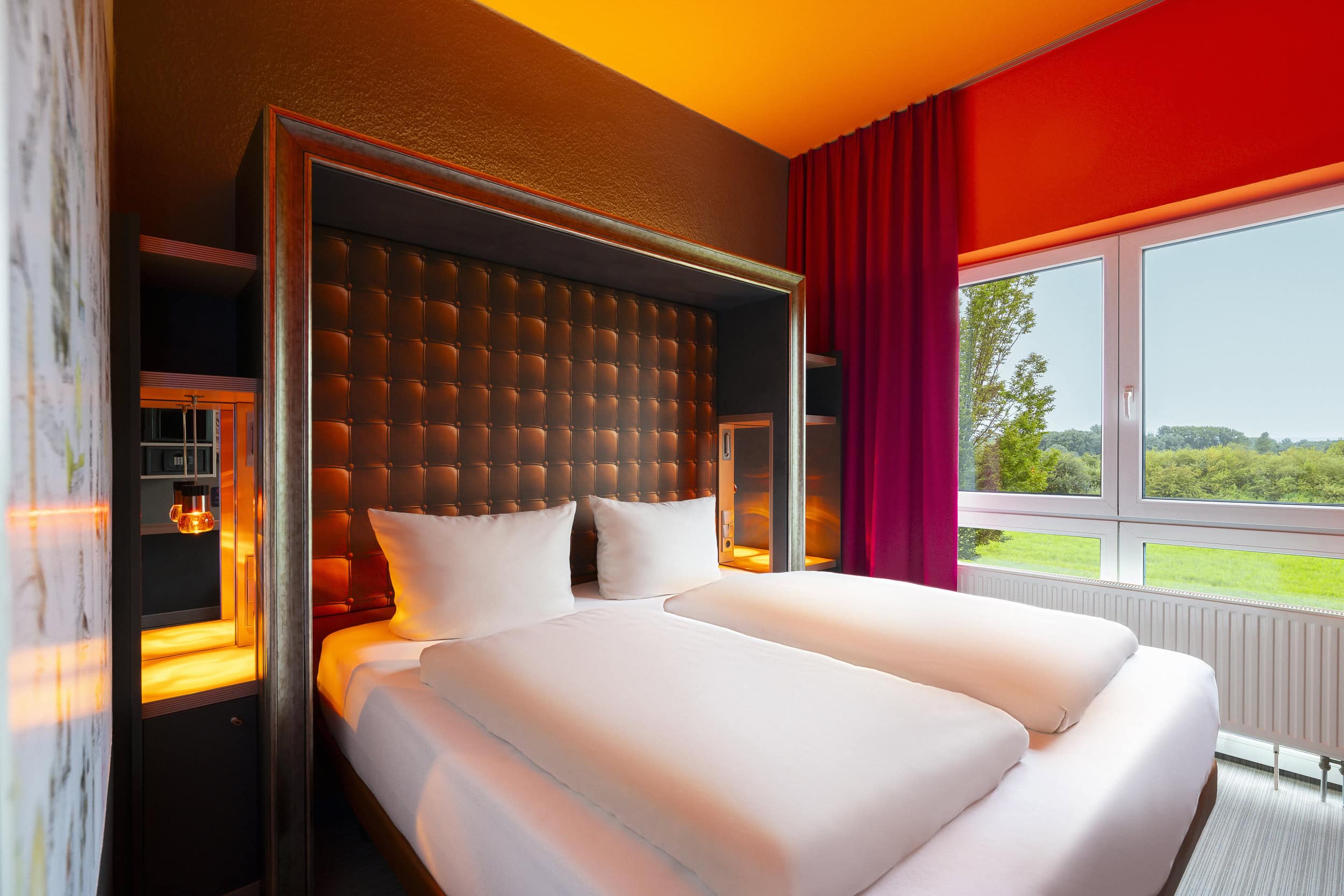 Hotelzimmer-Ansicht mit Blick auf das Bett und Fenster dahinter, mit offenen Vorhängen und Blick in das Landschaftsschutzgebiet.