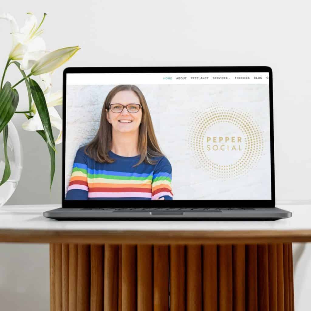 A cheerful woman wearing glasses and a vibrant rainbow-striped sweater, smiling across a modern workspace.