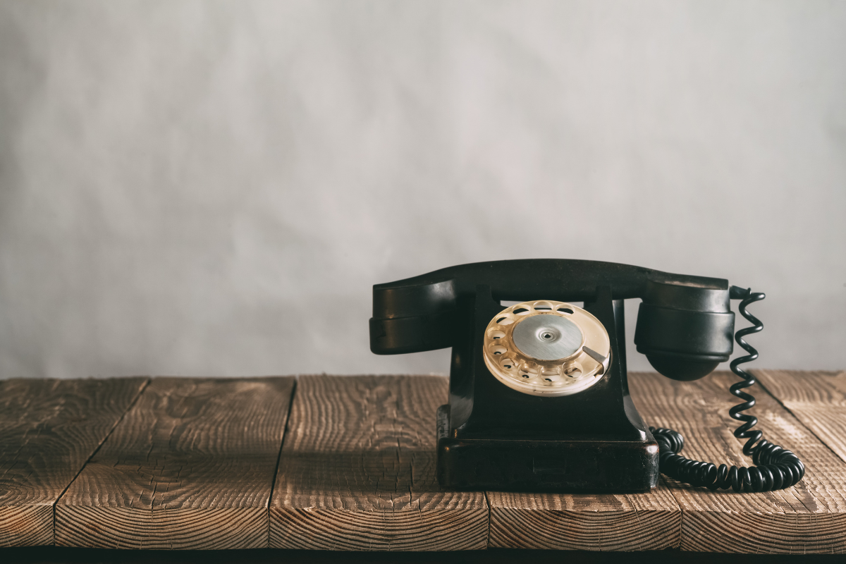 Vintage black rotary telephone on wooden table with neutral background.