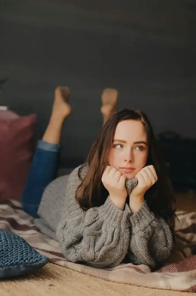a girl in her luteal phase lies on her bed with a sad expression on her face