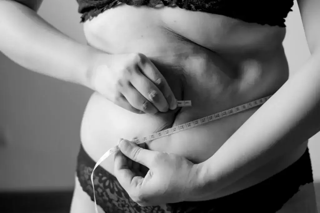 a woman wraps a measuring tape around her exposed middle to measure her waste size as her metabolism continues to slow down