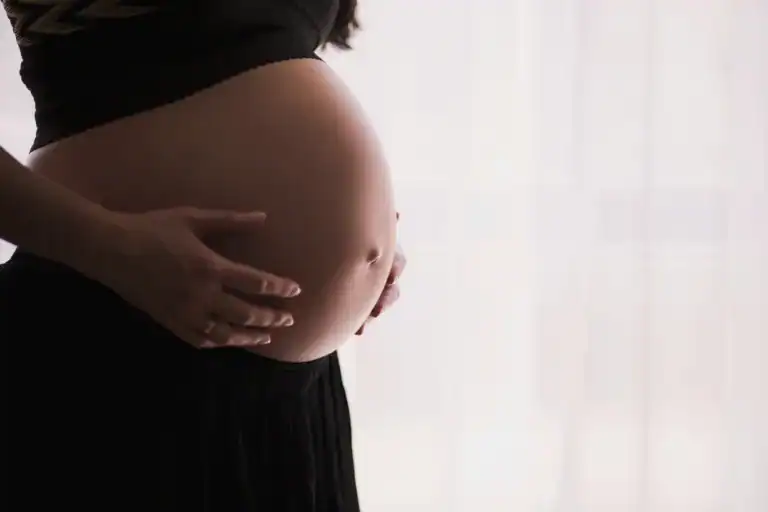 Pregnant woman gently holding her belly in a bright room.