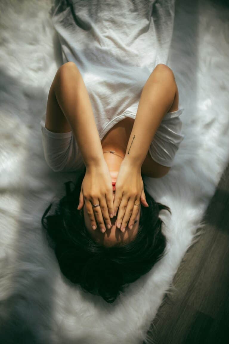 Woman lying down with her hands over her face from experiencing symptoms of being estrogen dominant