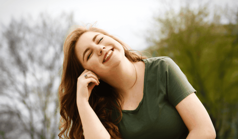 Joyful woman smiling outdoors in a green park or garden.