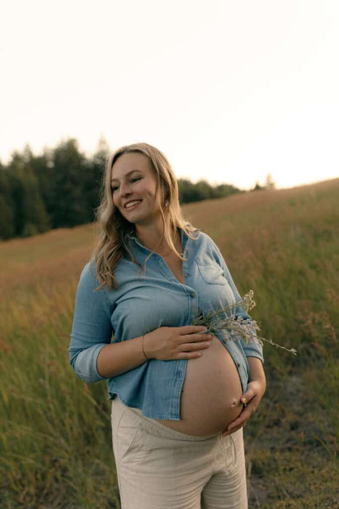 Pregnant woman smiling outdoors in a field during sunset.