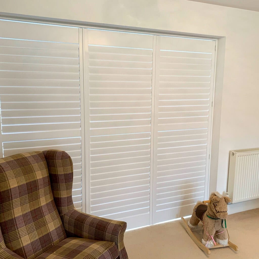 White plantation shutters controlling sunlight and helping keep a bright living room cooler during warm weather.